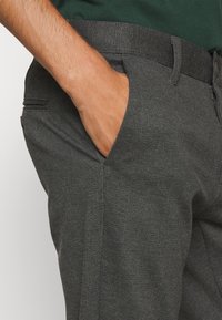 Szare spodnie wizytowe o teksturowanej tkaninie, dopasowanym kroju, gładkim przodzie i bocznych kieszeniach, z elastycznym pasem dla wygody.