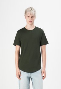 Dunkelgrünes Baumwoll-T-Shirt mit kurzen Ärmeln und Rundhalsausschnitt, mit geradem Saum und figurbetonter Silhouette. Trägt man mit hellblauen Jeans.