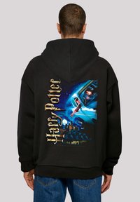 Fekete kapucnis pulóver, amelynek hátoldalán egy színes Harry Potter grafikát láthatunk, rajta karakterek és egy kastély a sötét ég alatt.