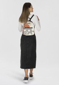 Vue arrière d'un petit sac à dos multicolore avec une base blanche, des pois noirs et un accent rose. Bretelles ajustables sur un modèle portant une jupe noire.