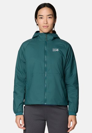 Person trägt eine türkisfarbene Mountain Hardwear Kapuzenjacke, die hochgeschlossen ist, und steht vor einem einfarbigen hellen Hintergrund.