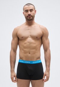 Cuecas pretas com um cós elástico azul, com o texto "JACK & JONES". O tecido parece liso e o design é justo ao corpo.