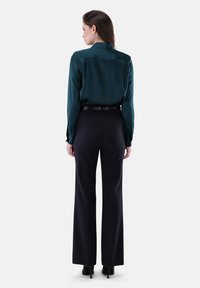 Blusa in satin di un blu scuro con colletto, abbinata a pantaloni neri a vita alta. I pantaloni sono a gamba dritta, con una texture liscia e dettagli minimi.