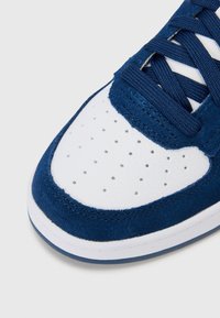 Blue suede and white leather sneaker featuring a perforated toe box, textured surface, and navy laces. White rubber outsole with navy accent.