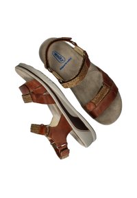 Brown leather sandals with braided accents, adjustable straps, and a cushioned sole. The design features a rounded toe and ergonomic shape.