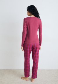 Burgunderfarget langermet topp med en tettsittende design, kombinert med rutete bukser i nyanser av burgunder og rosa. Myk tekstur med en avslappet passform.