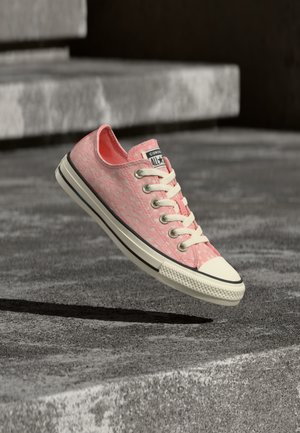 Pink lav sko Converse-sneaker med hvide snørebånd, hvid tåhætte og subtil leopardprint, der svæver over teksturerede betontrin.