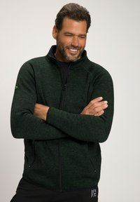 Giacca in pile verde con zip, caratterizzata da un motivo testurizzato, colletto alto e tasche con zip, con dettagli in contrasto neri.