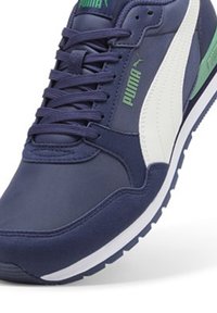 Baskets bleu marine avec des accents blancs et verts, présentant une tige synthétique texturée, un col rembourré et une semelle en caoutchouc avec un motif de traction.