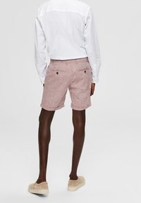 Shorts rayés rouges fabriqués dans un tissu léger, dotés de deux poches arrière et d'un ourlet roulé, associés à des chaussures beiges à enfiler et à une chemise blanche.