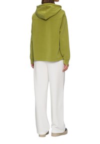 Sweatshirt à capuche vert avec une coupe décontractée et des manches longues, associé à un pantalon large blanc. Texture lisse et design minimaliste.