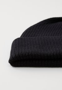 Bonnet en tricot noir, avec une texture côtelée et un revers replié. Le matériau est doux et épais, offrant chaleur et confort.