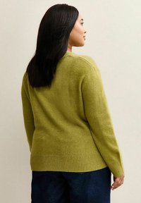 Olive zielony sweter wykonany z miękkiego materiału, z prążkowanym wykończeniem, okrągłym dekoltem i lekko oversize'owym krojem, w połączeniu z ciemnoniebieskimi dżinsami.