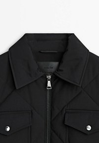 Zwarte gewatteerde jas met puntige kraag, vooraan met rits en twee klepzakken die zijn beveiligd met zilveren knopen.