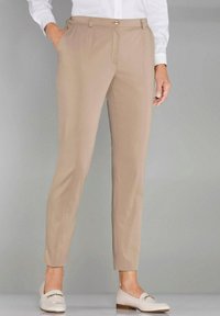 Pantalons beiges sur mesure en tissu léger, avec un devant plat, des poches latérales et une coupe slim. Assortis à des mocassins blanc cassé.