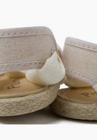 Sandalias de tela color beige claro con suela de esparto, que cuentan con suaves tiras de algodón y un pequeño acento metálico en la parte trasera.