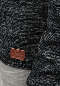 Grau gestrickter Pullover mit einem strukturierten Muster, versehen mit einem braunen Lederetikett, auf dem "BLEND GLOBAL JEANMAKER" steht, am unteren Rand.