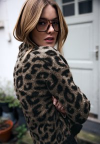 Płaszcz w panterkę wykonany z miękkiej, puszystej tkaniny w brązowych i czarnych odcieniach, o luźnym kroju i długich rękawach.