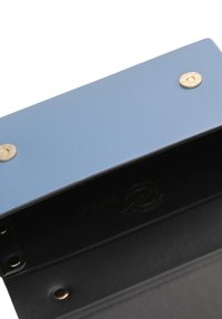 Portafoglio rigido blu con interno nero, dotato di bottoni a pressione in ottone e branding discreto sul lato interno. Dettaglio della superficie texturizzata visibile.