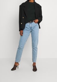 Blazer noir à double boutonnage, haut côtelé vert, jean taille haute bleu clair, et mules noires en résille avec bout pointu.