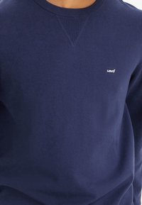 Mörkblå sweatshirt i bomullsblandning, med ribbad rundhals och en liten vit Levi's-logotyp på bröstet. Slät textur.