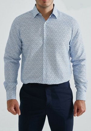 Chemise boutonnière bleu clair avec un motif floral en marine et blanc. Elle possède des manches longues et un col classique, fabriquée en tissu doux.