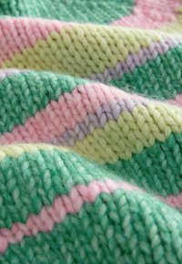 Strikket tæppe med sammenflettede grønne, pink, lavendel og lysegule garn. Blød tekstur med diagonale striber i forskellige bredder.