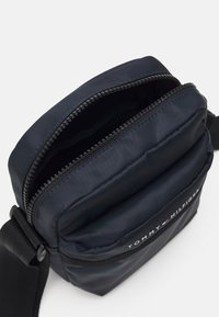 Marinblå nylon axelväska med ett framfack med blixtlås och svarta detaljer. Har en mjuk textur och en logotypdetalj på framsidan.