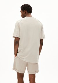 Beige T-shirt met korte mouwen en een ontspannen pasvorm, met raglanmouwen en zachte, geweven stof. G gedragen met bijpassende shorts.