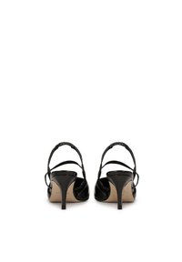 Black patent leather heels with a slender ankle strap, a pointed toe, and a low stiletto heel. The interior features a neutral lining.