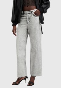 Jeans de mezclilla gris de pierna ancha con una cintura alta, que presentan un dobladillo deshilachado y bolsillos frontales. Combinados con tacones negros de tiras y una camiseta corta.