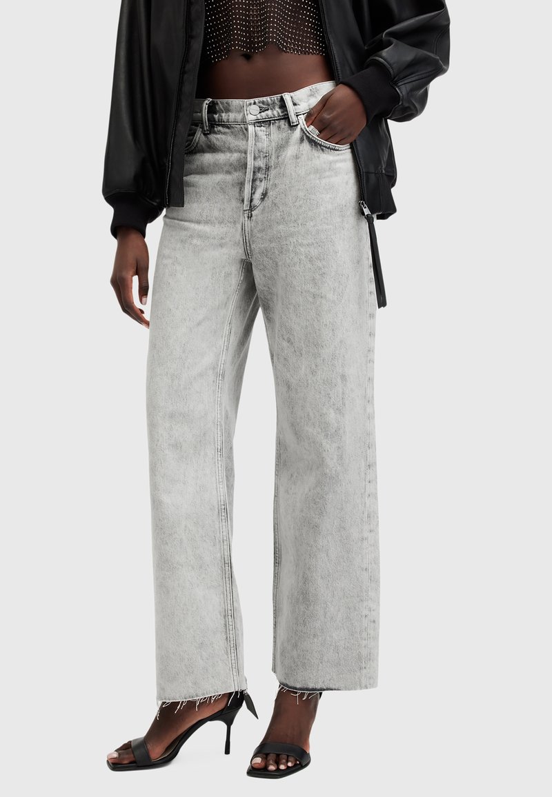 Jeans de mezclilla gris de pierna ancha con una cintura alta, que presentan un dobladillo deshilachado y bolsillos frontales. Combinados con tacones negros de tiras y una camiseta corta.