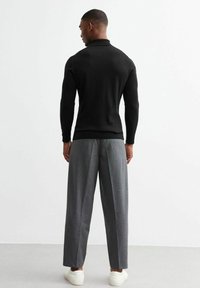 Polo negro de punto con cuello alto, combinado con pantalones sueltos de cuadros grises y zapatillas blancas, visto desde la espalda.