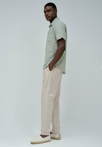Camisa de manga corta verde claro con un bolsillo en el pecho, combinada con pantalones beige claros y zapatos espadrilles blancos. Tejido suave y corte relajado.