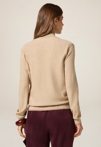 Maglione beige a maglia con scollatura rotonda e maniche lunghe, dotato di bordo e polsini a coste, abbinato a pantaloni in velluto a coste viola scuro.