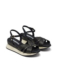 Sandalias de cuña negras con tiras de textil trenzadas, diseño de punta abierta, correa ajustable en el tobillo y una suela de color claro en contraste.