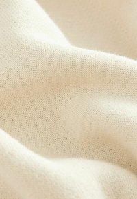 Cream-colored knit fabric with a fine, soft texture and a smooth appearance, showcasing small, evenly spaced stitches throughout.