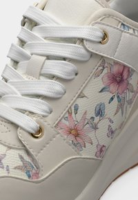 Baskets blanches avec des lacets épais, des œillets dorés et un motif floral comprenant des fleurs roses et bleues sur des panneaux latéraux texturés.