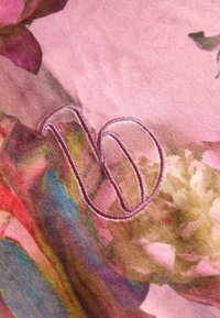 Kvetinový vzor na látke v ružovo-fialovej farebnej škále s vyšívaným písmenom "V" v svetloružovej farbe. Mäkká textúra, detailný a zložitý dizajn.