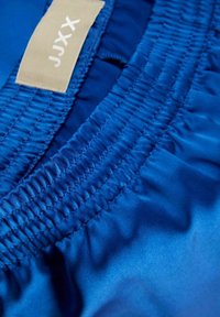 Close-up of blue elastic waistband on clothing with beige label marked "JJXX" stitched inside.