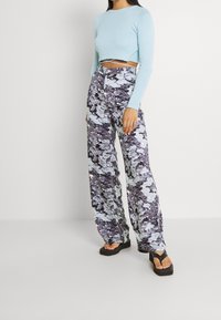 Przycięty, jasnoniebieski, długi rękaw top, połączony z szerokimi spodniami w wzory w odcieniach fioletu, szarości i bieli. Czarne klapki na platformie.