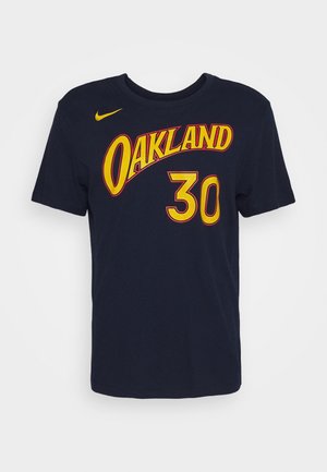 Camiseta azul marino con texto "OAKLAND" en amarillo y rojo en el pecho, número "30" en amarillo debajo, y pequeño logo de Nike en amarillo en el hombro derecho.