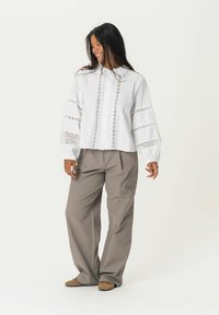 White cropped blouse with intricate lace detailing on sleeves and front. Paired with loose beige trousers and brown shoes.
