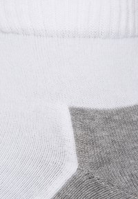 Tejido de punto blanco y gris que muestra una textura acanalada; presenta una transición sin costuras de áreas blancas a grises con diferentes patrones de punto.