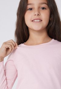 Svetle růžová dlouhá košile s dlouhým rukávem, vyrobená z měkké tkaniny, s kulatým výstřihem a mírným elastickým efektem, hladkým povrchem a přiléhajícími rukávy.