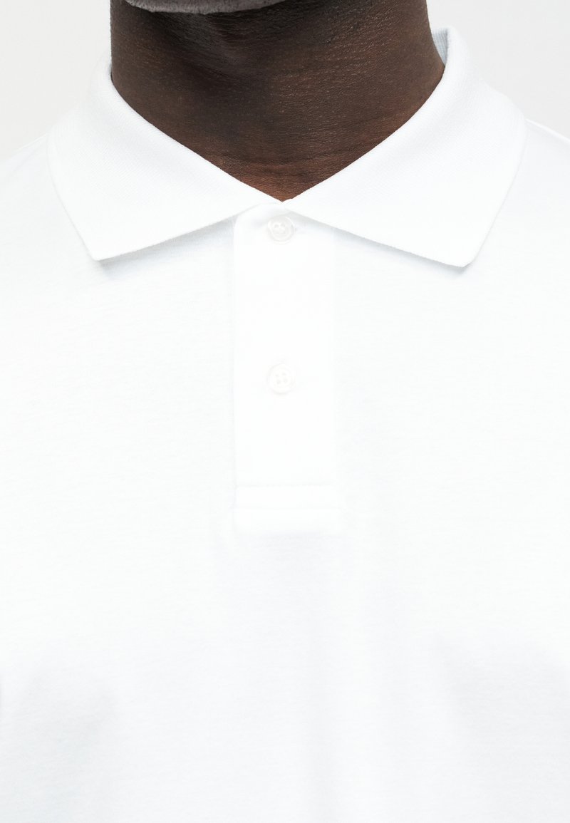 Dark-skinned person wearing a clean, white polo shirt with a buttoned collar.