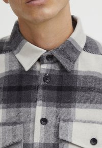 Grijs en wit geruite flanellen shirt met een puntige kraag, zwarte knopen en twee zaklapjes. Zachte textuur met een relaxte pasvorm.