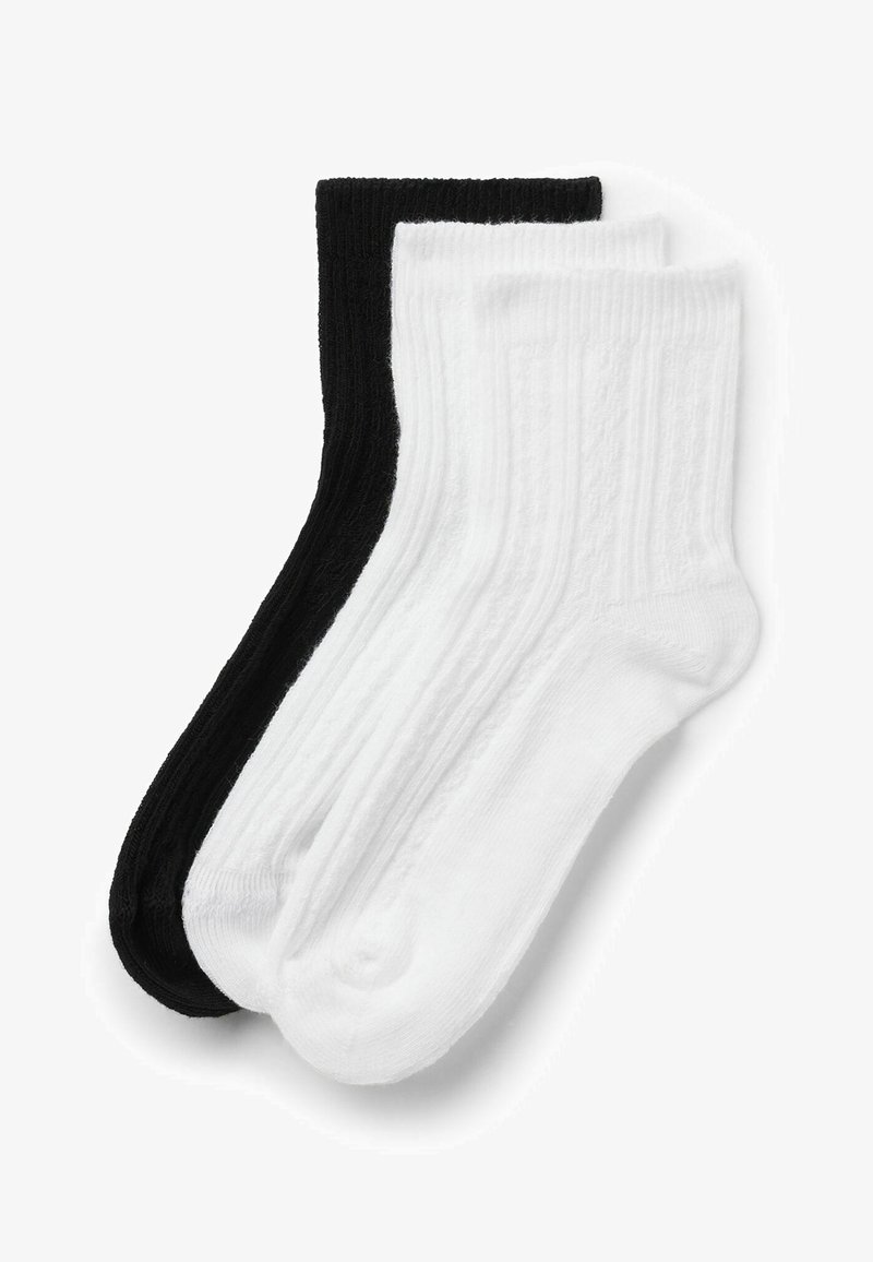 Deux paires de chaussettes côtelées mi-mollet, une noire et une blanche, posées à plat et se chevauchant sur un fond blanc.