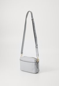 Borsa a tracolla in pelle grigia con chiusura a zip e tracolla regolabile. Presenta hardware in tonalità oro e una texture liscia. Forma rettangolare compatta.