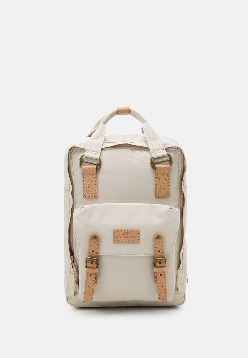 Beige backpack with a rectangular shape, leather accents, front pocket, adjustable straps, and metal hardware detail. Textured fabric exterior.